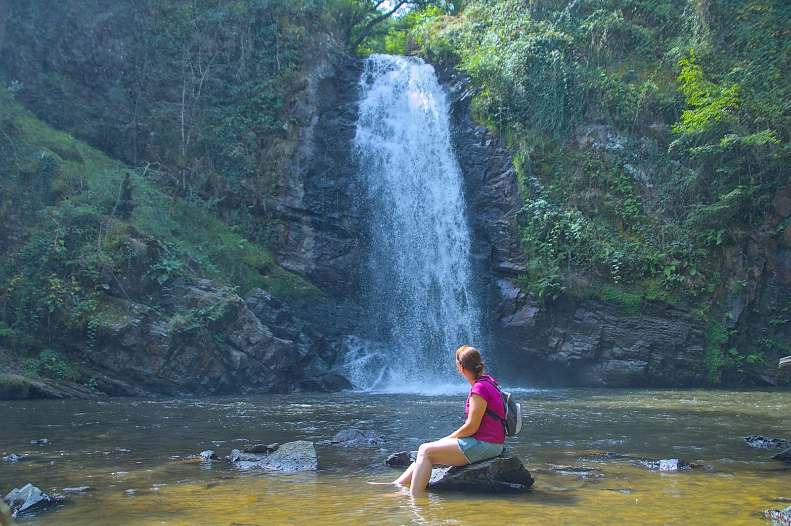 Hiker seated by a forest waterfall